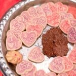 Heart-shaped cookies with pink icing reading "Kiss Me," "I Love You," "Be Mine," and "XOXO" on a silver platter.