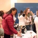 A woman in a red puffer jacket browses a bridal show vendor table with wedding gowns and jewelry on display.