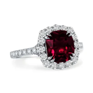 A silver engagement ring with a deep red cushion-cut ruby center surrounded by a halo of small white diamonds.