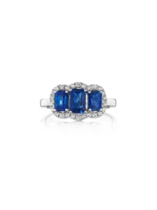 A white gold ring with three emerald-cut blue sapphires framed by a halo of small round diamonds.